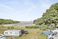First Camp Malmö- Zelt- und Wohnwagenstellplätze zwischen Weg und See auf der Wiese der Campingplatzanlage